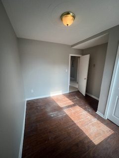A bedroom with grey walls and afternoon sun across a dark wood-look floor
