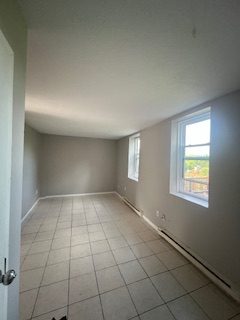 A long living room with grey walls, white baseboards and two windows