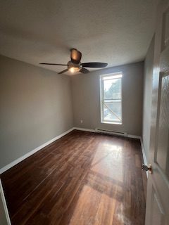 A bedroom corner with grey walls, a window and a ceiling fan